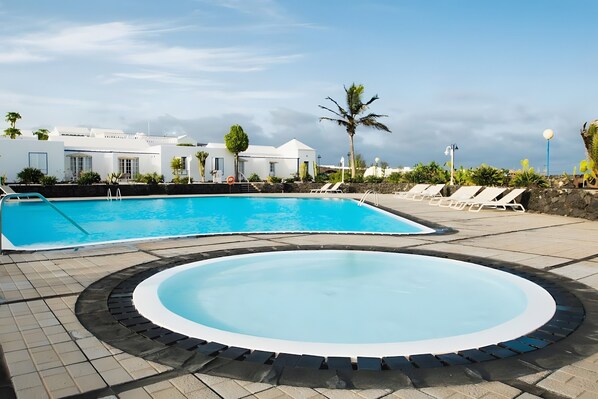 Una piscina con un jacuzzi circular, sillas de descanso y un edificio de fachada blanca.