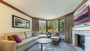 A cozy living room with a fireplace, a large window with curtains, a sofa, and a coffee table. - Resort at Squaw Creek Tahoe Hyatt 2Bd/2Ba Fireplace Suite (Olympic Valley)