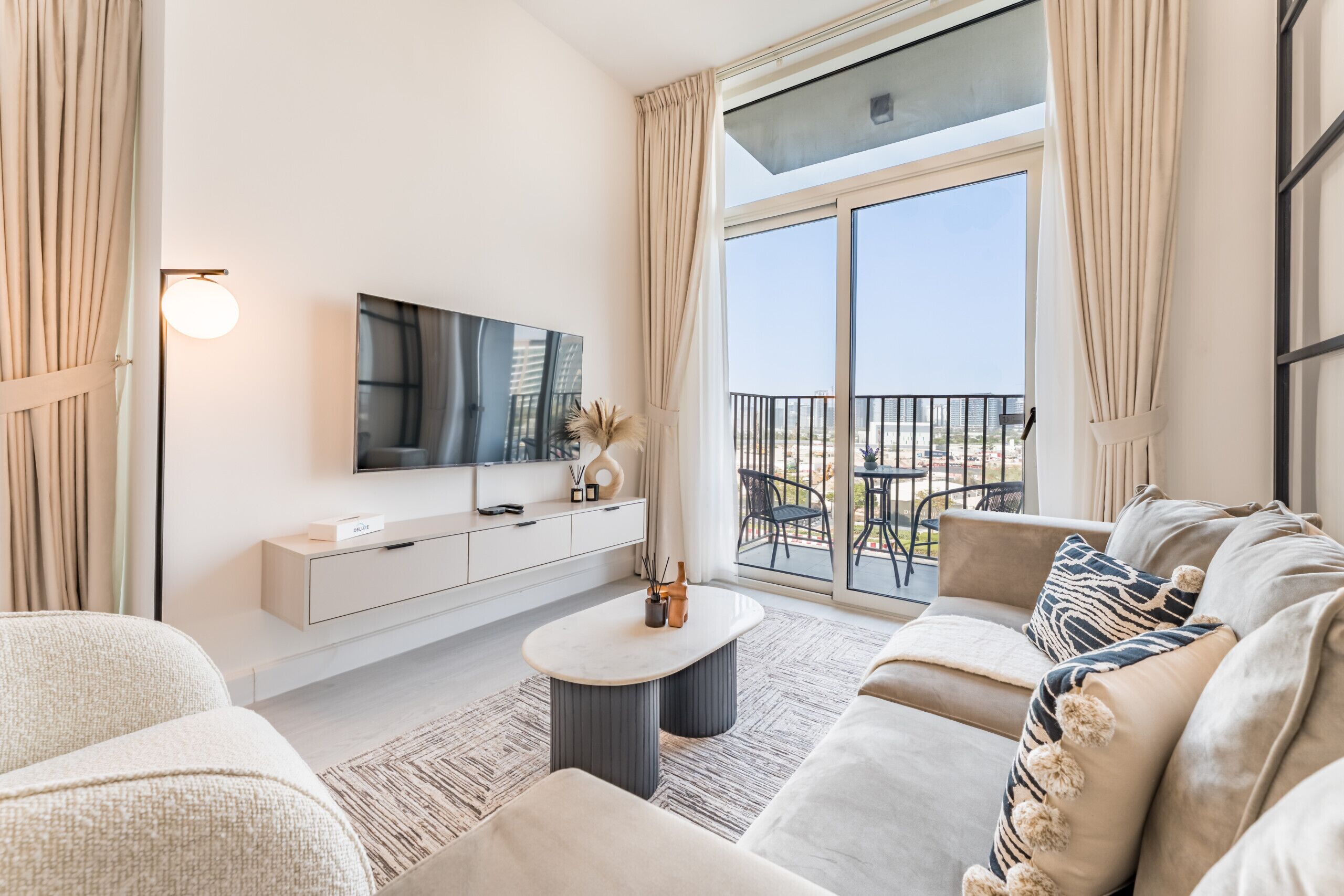 A modern living room with a large TV, comfortable seating, a balcony with outdoor furniture, and a minimalist design.
