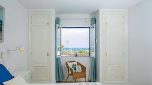 Een slaapkamer met een bed, een stoel, een raam met gordijnen en uitzicht op zee.