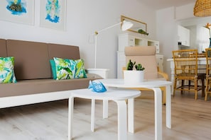 A modern living room with a sofa, a coffee table, a lamp, and a dining area with chairs.