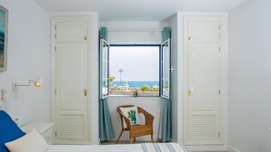 Un dormitorio con cama, una silla, ventana con cortinas y vista al mar.