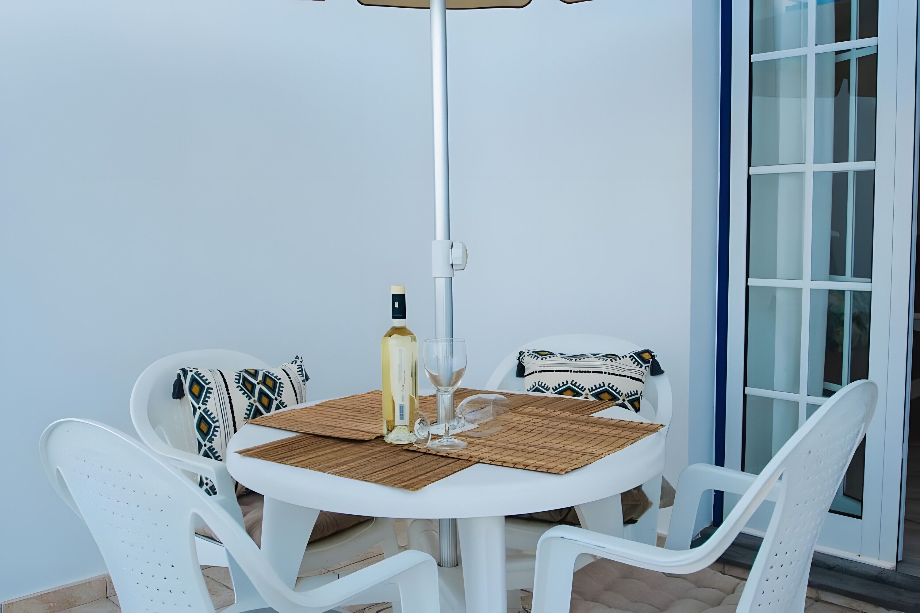 A round table with chairs, a bottle, and a glass on a woven placemat.