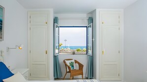 A bedroom with a bed, a chair, a window with curtains, and a view of the sea.