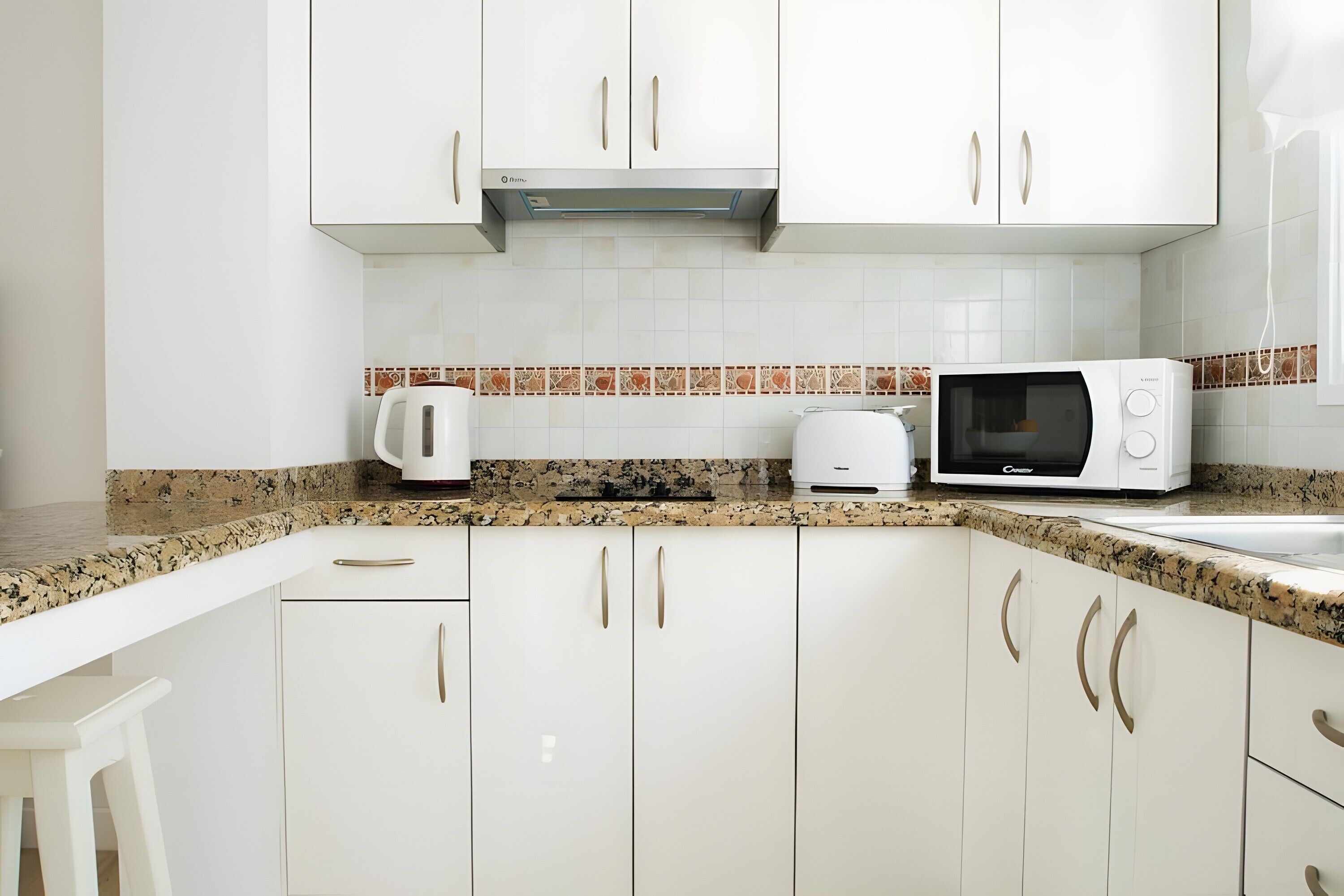 A kitchen with white cabinets, a microwave, a kettle, and a toaster.