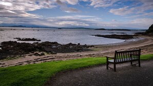 A bench overlooking a rocky shoreline with a view of the sea and distant hills.