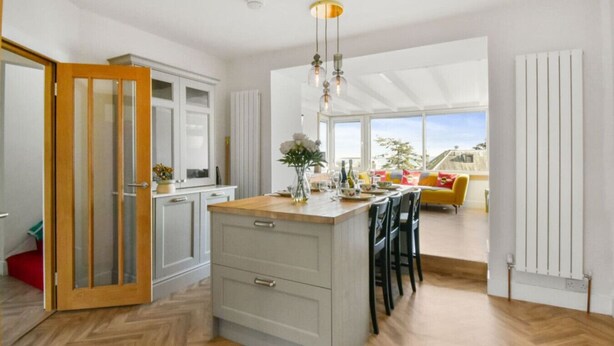 A modern kitchen with a central island, wooden flooring, and a view to a bright living area.