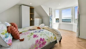 A bedroom with a large bed, a wardrobe, a desk, and a view of the sea.