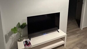 A modern living room with a flat-screen TV on a white stand, two framed pictures on the wall, and a small plant on the stand. - 2 persons apartment, Julianadorp (Willemstad)