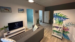 A modern living room with a flat-screen TV, grey sofa, and a decorative plant. - 2 persons apartment, Julianadorp (Willemstad)
