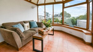 A cozy living room with a brown sofa, blue cushions, a wooden coffee table, and a view through large windows. - Blacksands Seaview Cottage, Aberdour (Aberdour)