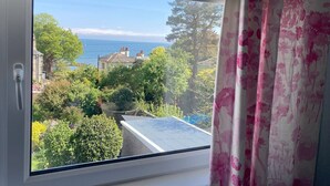A view from a window with a view of a house, trees, and a body of water. - Blacksands Seaview Cottage, Aberdour (Aberdour)