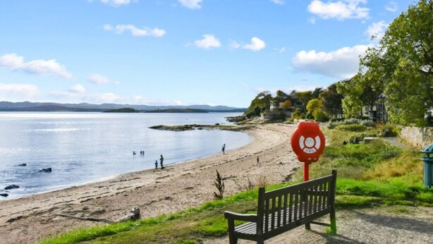 A bench and a red sign near a beach with people in the water. - Blacksands Seaview Cottage, Aberdour (Aberdour)