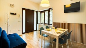 Een moderne eethoek met een tafel voor vier personen, een blauwe bank en een tv die aan de muur is bevestigd.