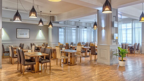 A spacious dining area with multiple tables and chairs, large windows, and pendant lighting. - Hotel Mevora (Tbilisi)