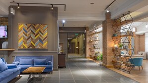 A modern lobby with a blue sofa, a wooden coffee table, a herringbone-patterned wall, and a brick accent wall with shelves. - Hotel Mevora (Tbilisi)