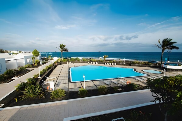 Une piscine avec vue sur l’océan, entourée de palmiers et de chaises longues.