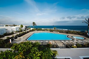 A swimming pool with lounge chairs and a view of the ocean. - Holiday Home 'Caleta Campos Bungalows' with Sea View, Shared Pool and Wi-Fi (Arrieta)