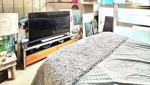 A room with a bed, a television on a wooden stand, a mirror, and a window with a metal roof. - Arty Infused Loft With ac Near Emirates Stadium (London)