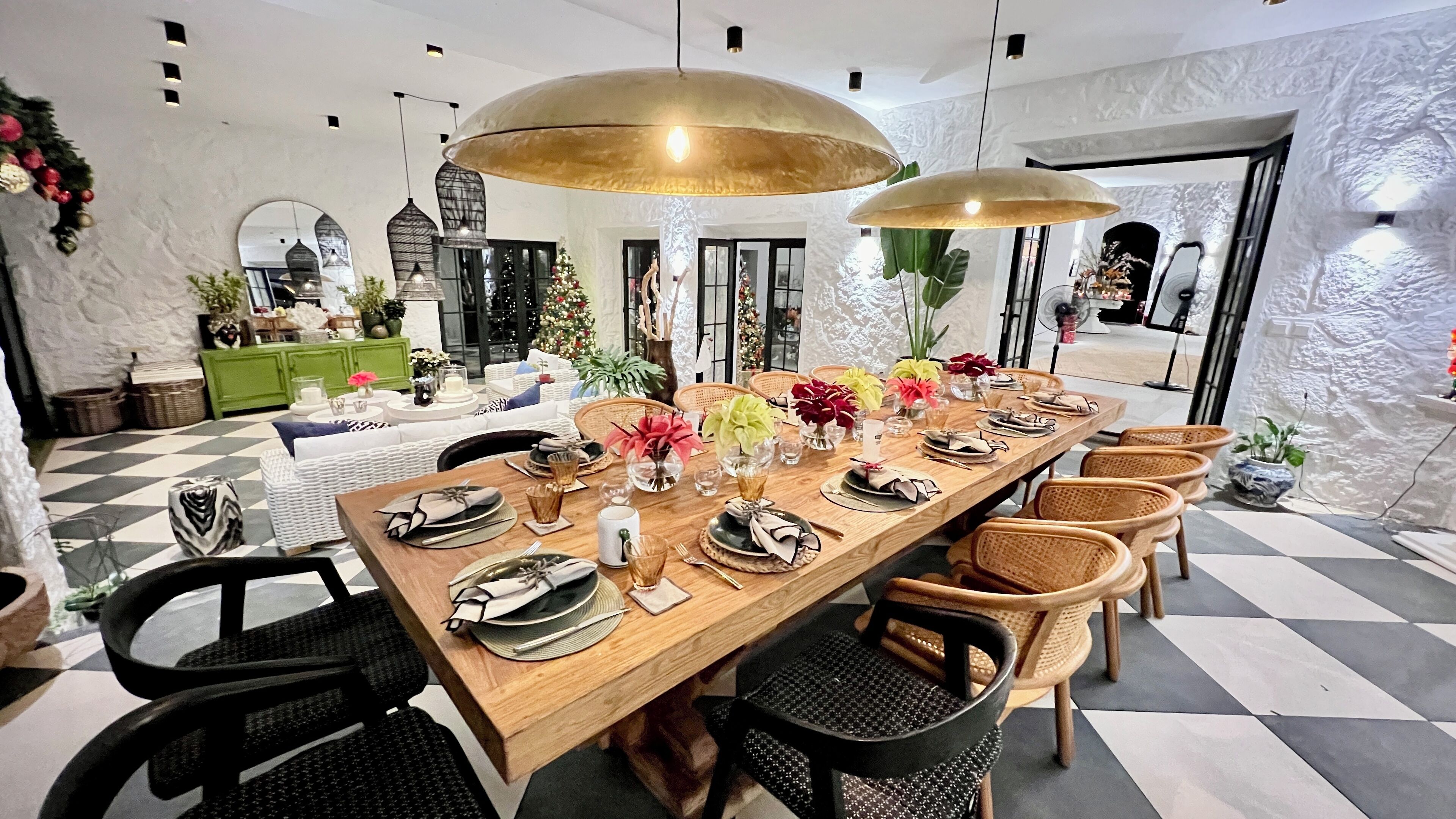 A dining area with a long wooden table set for a meal, surrounded by wicker chairs.
