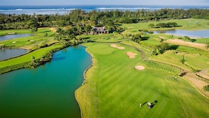 En golfbana med dammar, ett klubbhus och utsikt över havet.