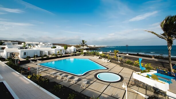 A swimming pool with lounge chairs, a smaller pool, and a view of the ocean.