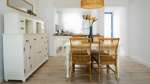A dining area with a white cabinet, wicker chairs, a table, and a hanging light fixture.