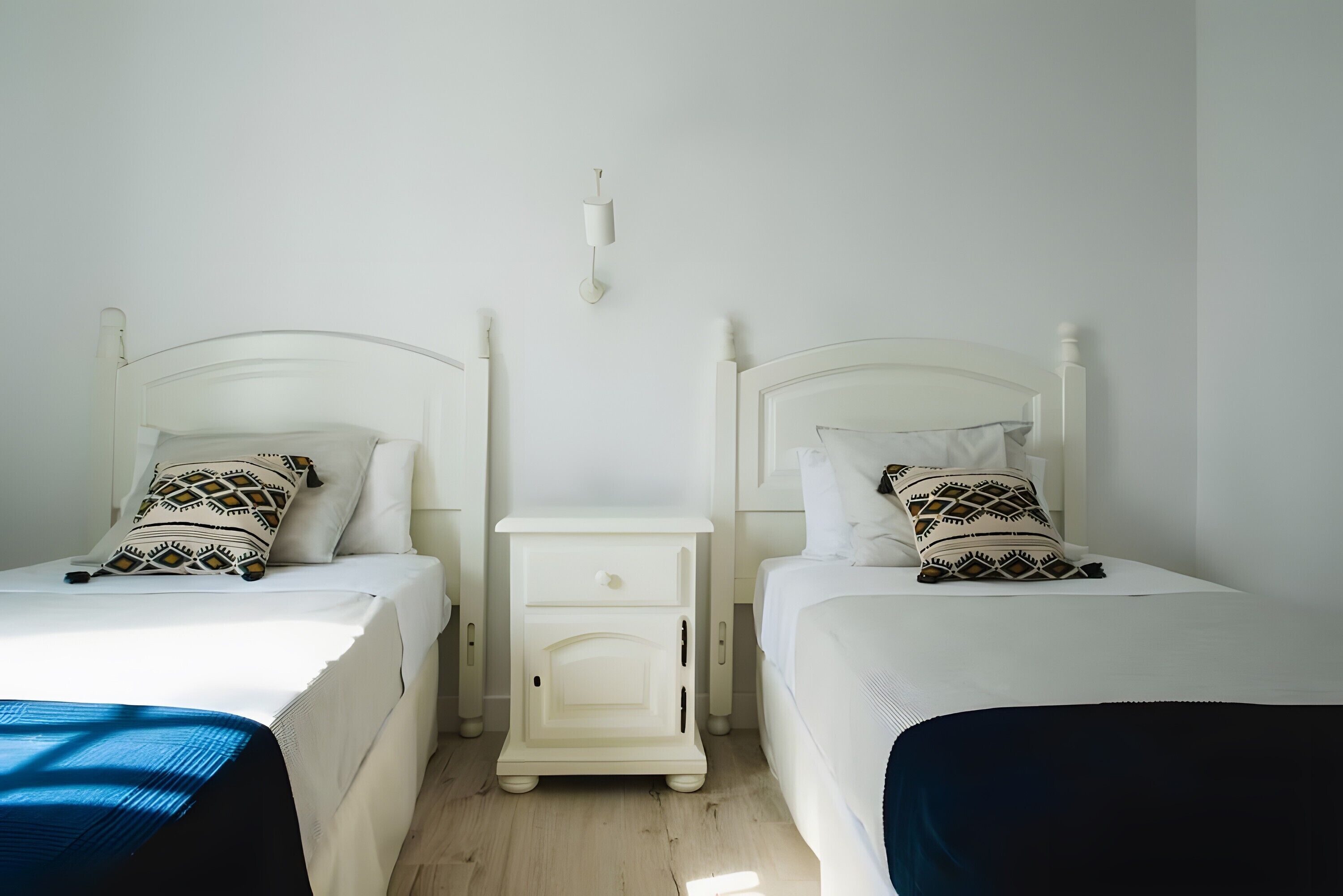 Two single beds with white headboards, a small bedside table, and a wall-mounted light fixture.