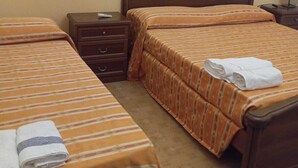 Une chambre d’hôtel avec deux lits simples, chacun doté de draps à rayures et d’une serviette pliée. On y trouve une table de chevet en bois avec une lampe et un tiroir.