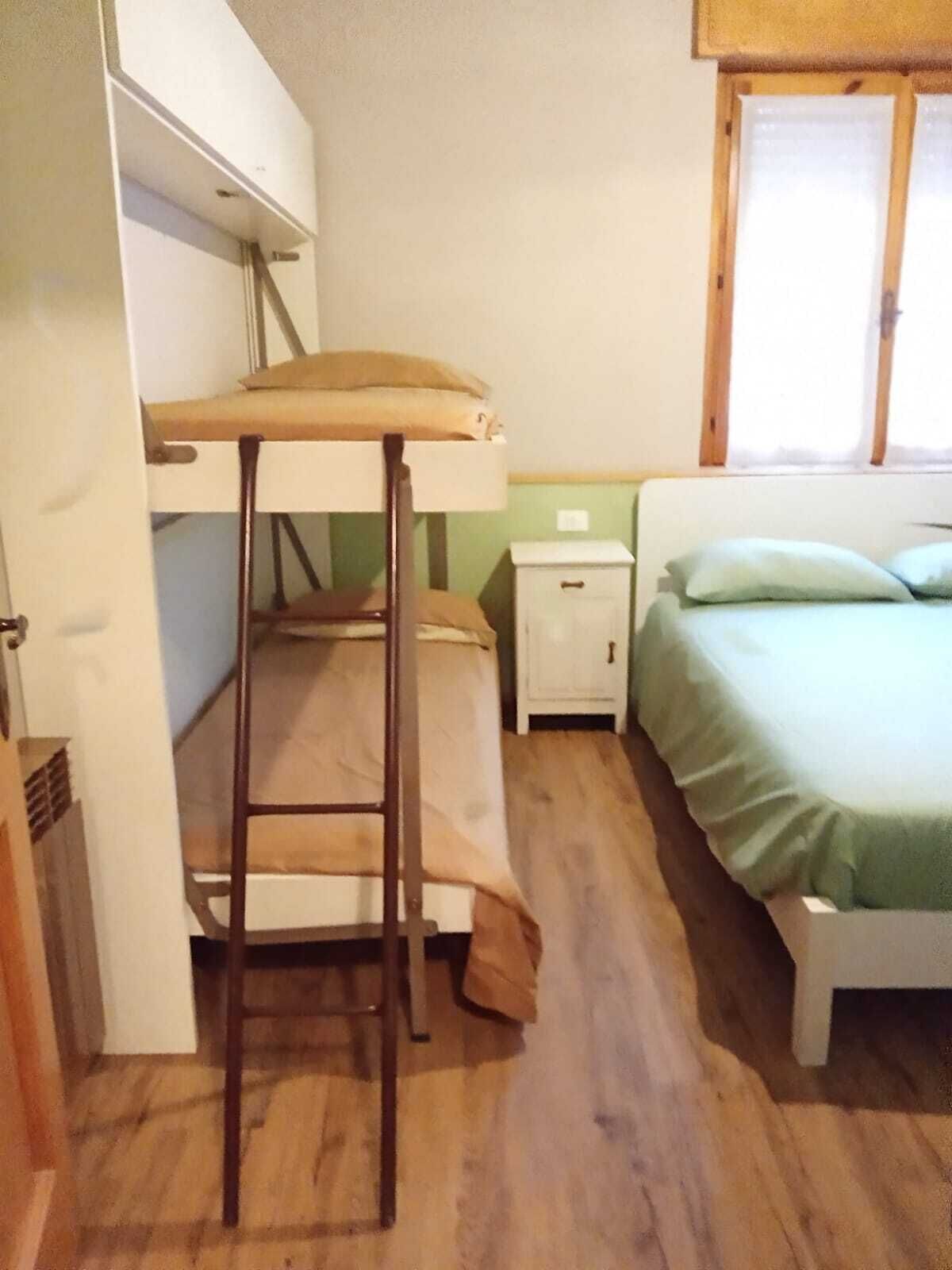Quarto compacto com cama de solteiro, uma pequena mesa de cabeceira e janela com persianas.