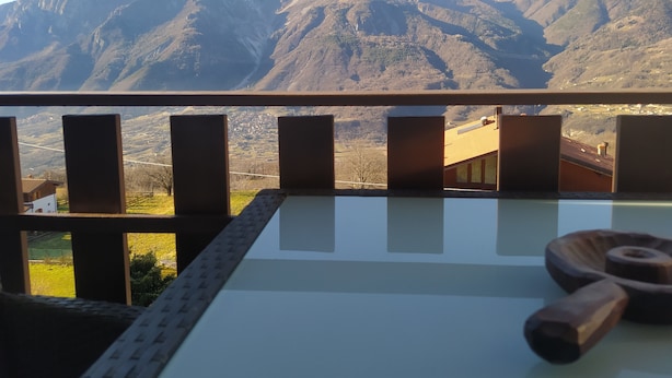 A balcony with a mountain view, a glass table, and wooden furniture. - Real Italy Retreat: Village, Views & Silence (Cimbergo)