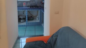 A narrow kitchen with a window, blue tiles, a gas stove, and a sink.