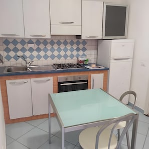 Una cucina compatta con mobili bianchi, una schiena blu e bianca, un fornello a gas, un lavandino e un piccolo tavolo con una sedia.