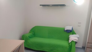 Ein Zimmer mit einem grünen Sofa, einem kleinen Tisch und einem Schrank.