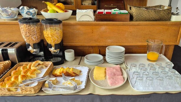 A buffet setup with various food items, including bread, pastries, and a fruit bowl. - Albergue La Pinguina (Mansilla de las Mulas)