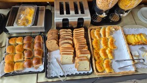 A buffet setup with various breads, rolls, and pastries. - Albergue La Pinguina (Mansilla de las Mulas)