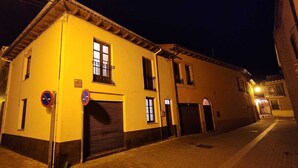 A two-story building with a yellow facade, a closed garage door, and a no parking sign. - Albergue La Pinguina (Mansilla de las Mulas)