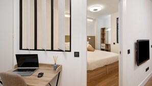 A bedroom with a bed, a desk with a laptop, a chair, a TV, and a mirror.