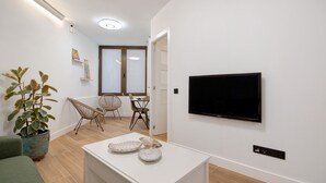 A modern living room with a flat-screen TV, a dining area with chairs, a potted plant, and a white console table.