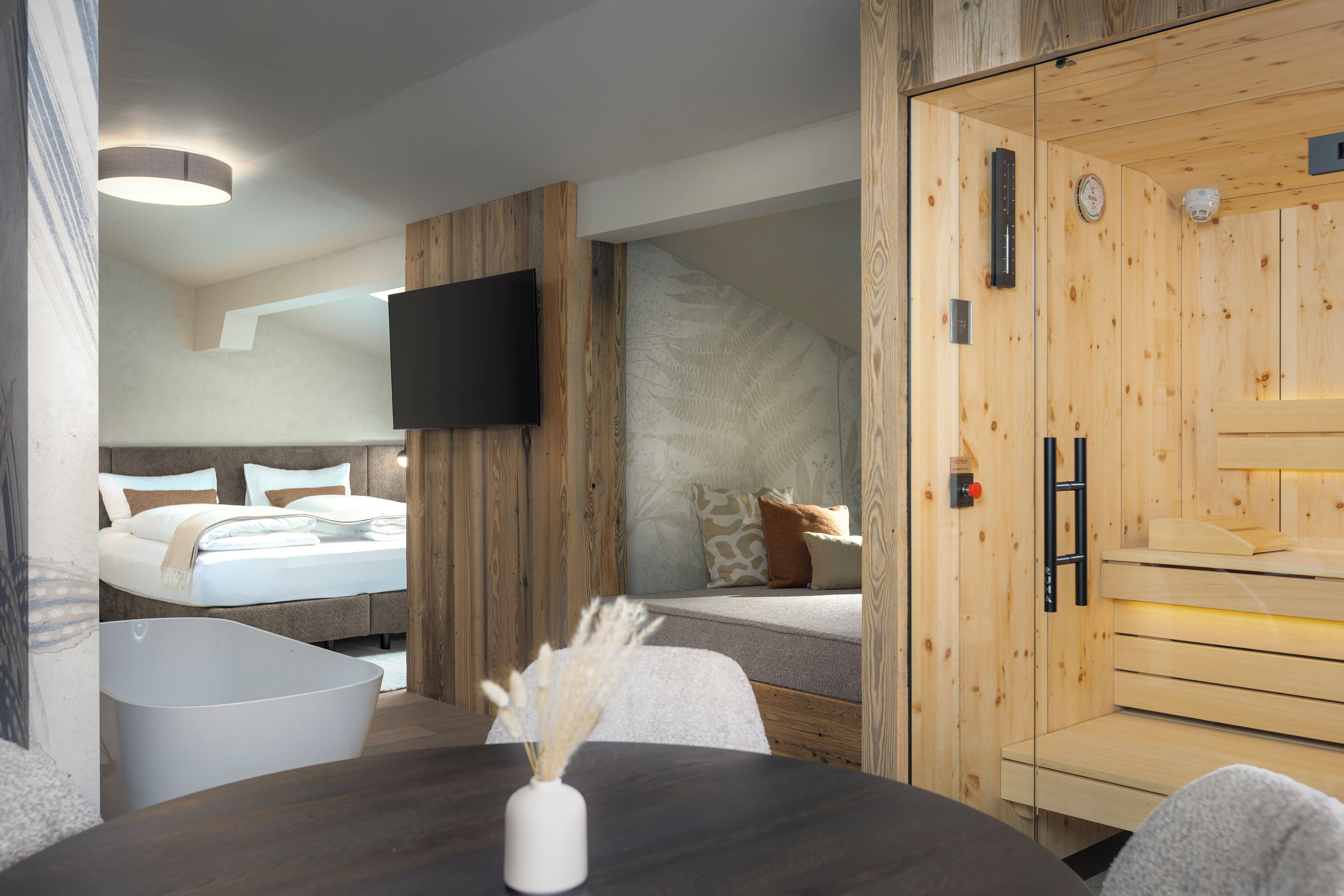 Une chambre d’hôtel moderne avec un intérieur en bois, un téléviseur à écran plat fixé au mur, un lit avec une literie blanche et un espace sauna.