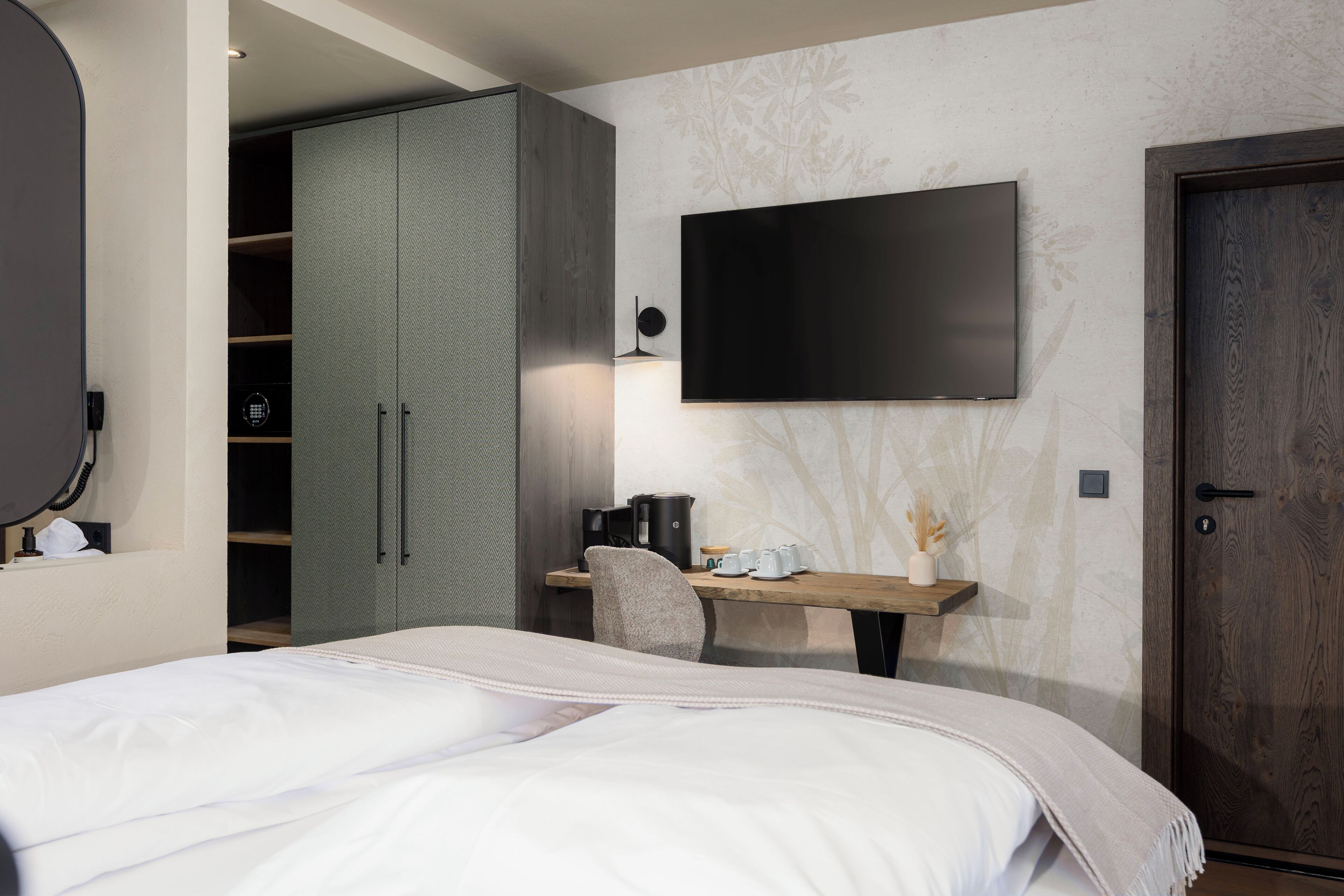 A bedroom with a bed, a desk, a chair, a wardrobe, and a TV mounted on the wall.