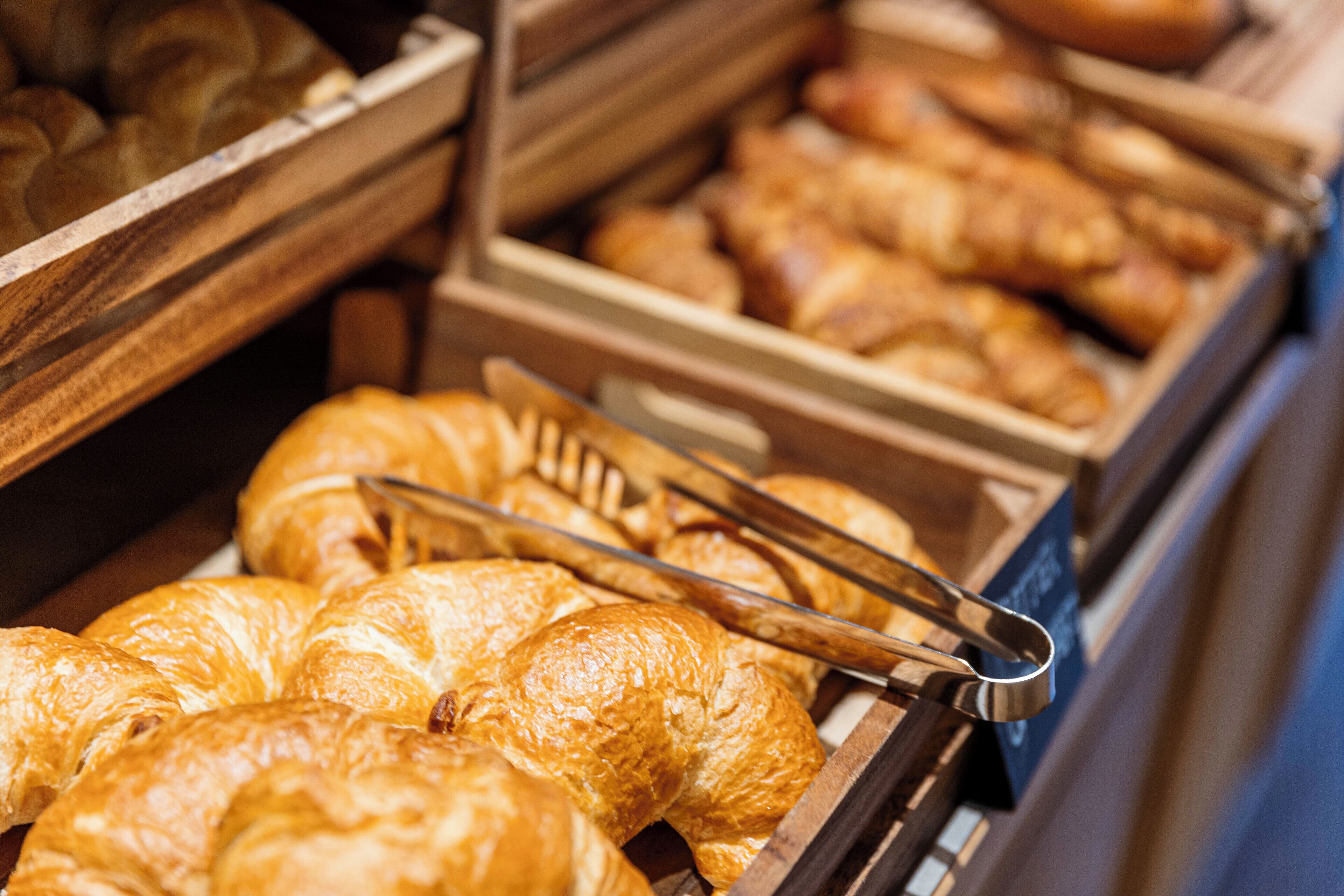 Una vitrina de panadería con diversos productos horneados, incluyendo cruasanes y pan, dispuestos en cajas de madera.