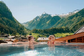 A swimming pool with two people, surrounded by mountains and houses.