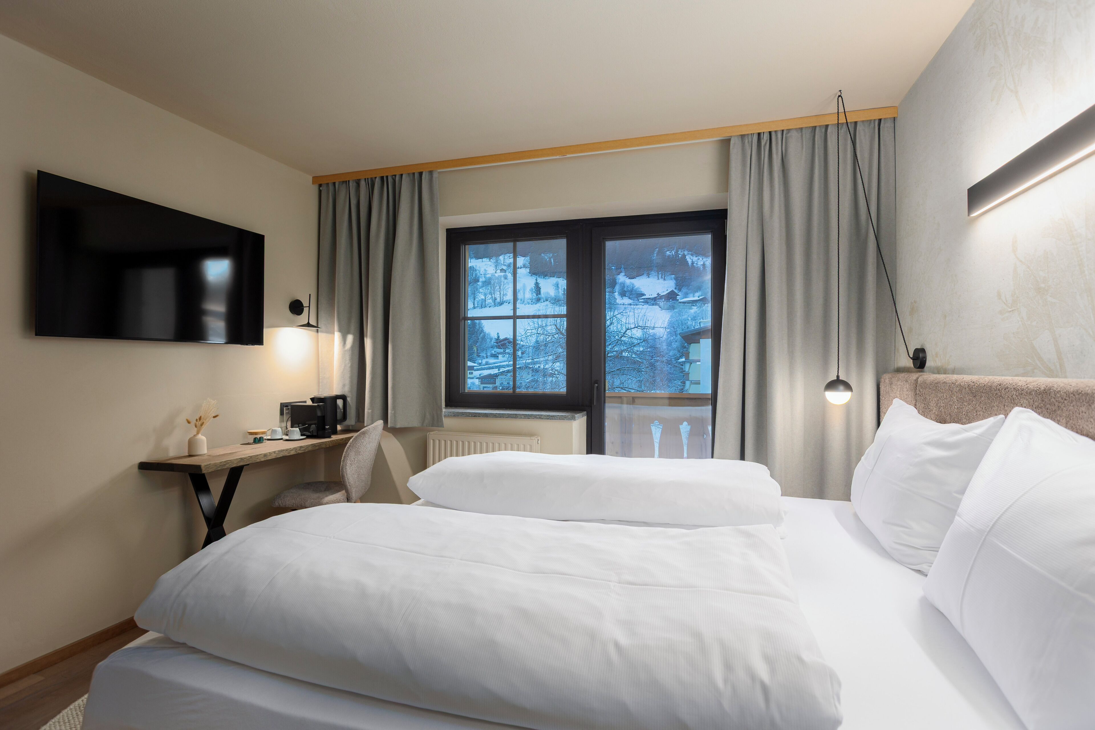 A hotel room with a large bed, a desk with a computer, a flat-screen TV, and a window with curtains.