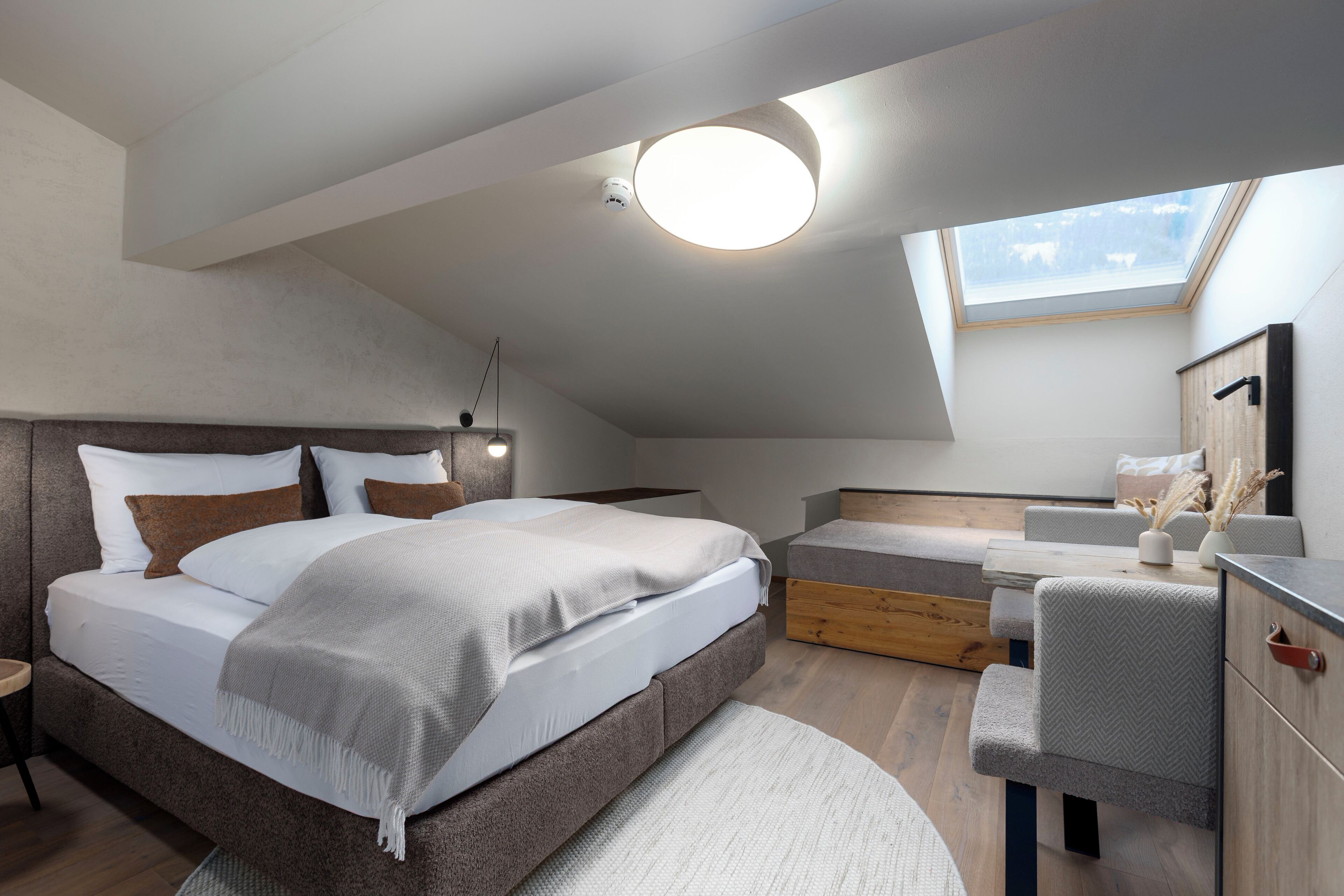 Une chambre moderne avec un plafond de style industriel, un grand lit, un coin salon et une lucarne.