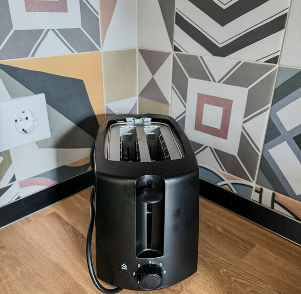 A black toaster on a wooden surface with a patterned wall in the background. - Luxury 3BR Apartment Near Basilica & Parliament (Budapest)