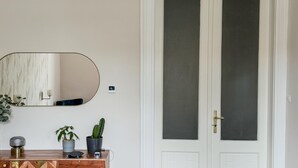 A bathroom with a white door, a round mirror, a small potted plant, and a wall-mounted air conditioner.