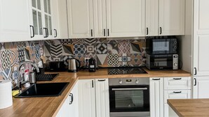 A modern kitchen with white cabinets, a patterned backsplash, a microwave, a coffee maker, and an oven.