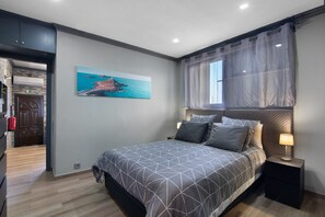 Une chambre à coucher avec un lit, une table de chevet, un tableau et une fenêtre avec des rideaux.