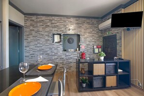 A modern dining area with a brick-patterned wall, a clock, and a television mounted above a dark console with baskets.